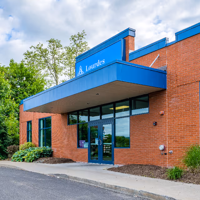 Red brick Lourdes Home Care building exterior with blue awning and glass entrance.