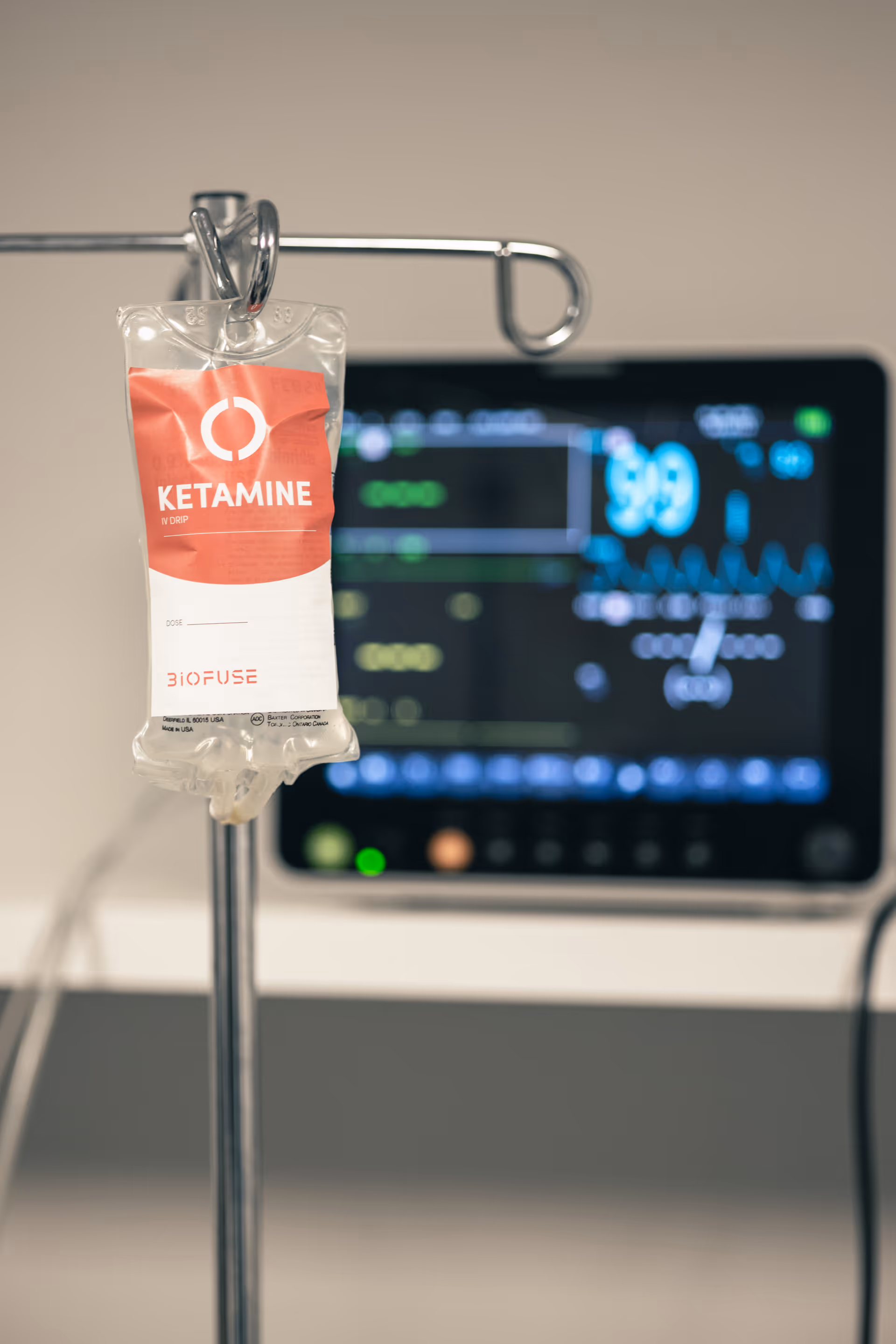 Close-up of an IV bag labeled Ketamine hanging on a medical pole in a clinical room.