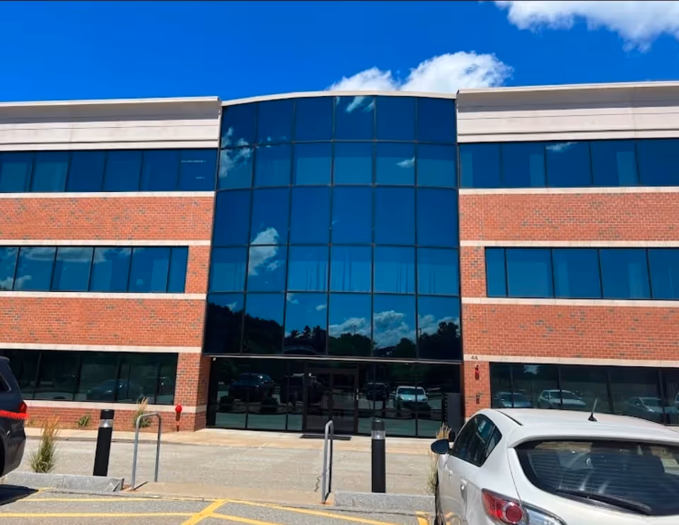 Brick-and-glass senior living facility exterior with a central glass entrance and parked cars.