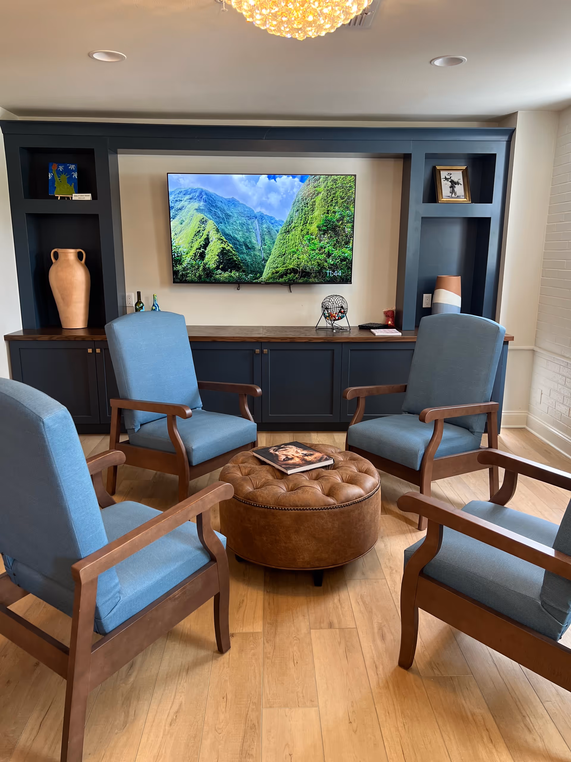 Lounge area with blue chairs, a tufted ottoman, and a wall-mounted TV.