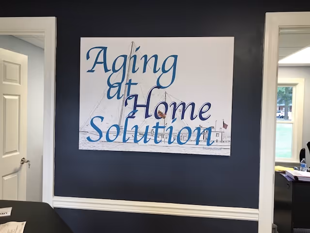 Large sign reading Aging at Home Solution mounted on a dark interior wall.