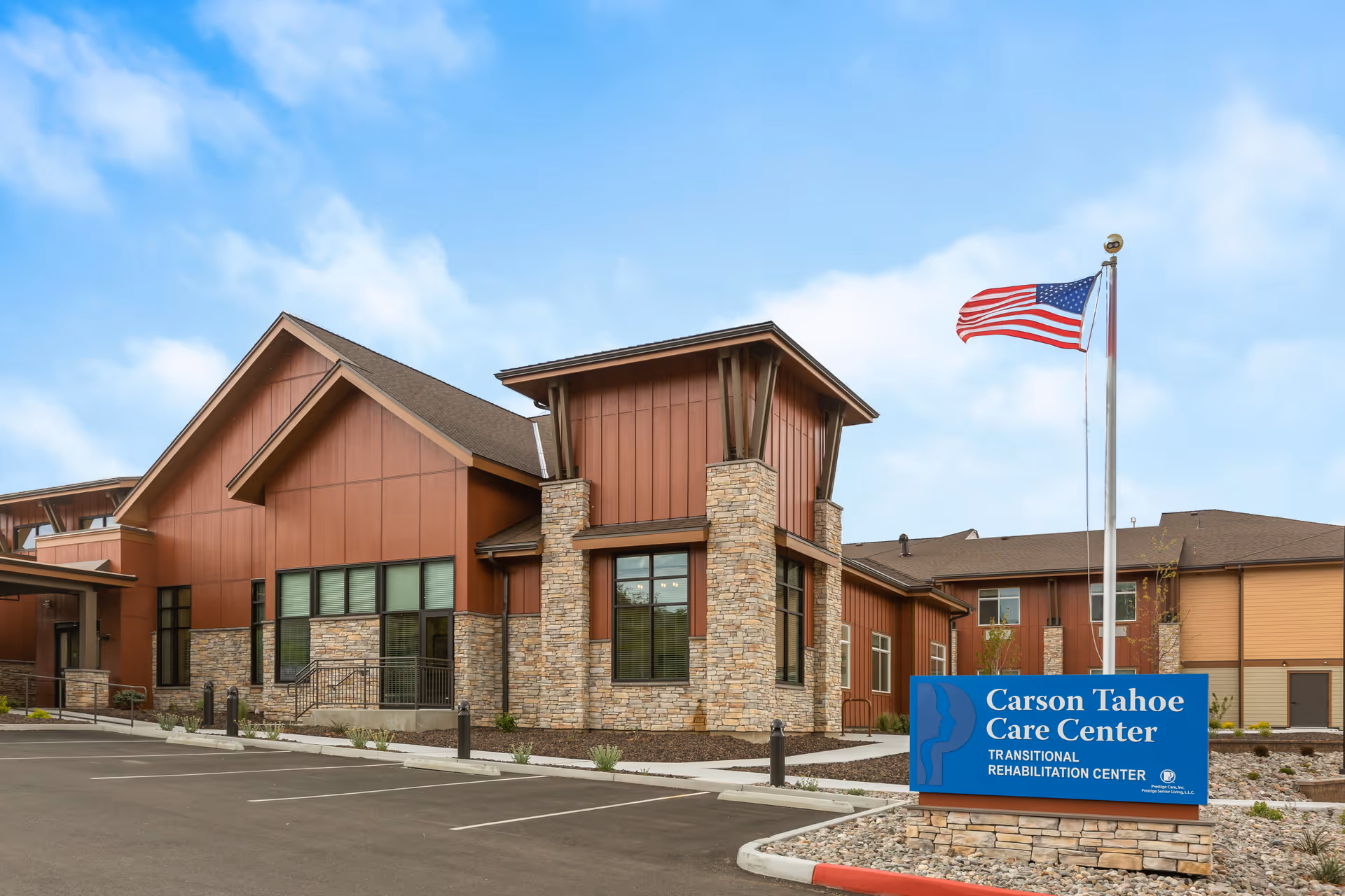 Exterior view of a memory care facility with red siding, stone accents, and an American flag.