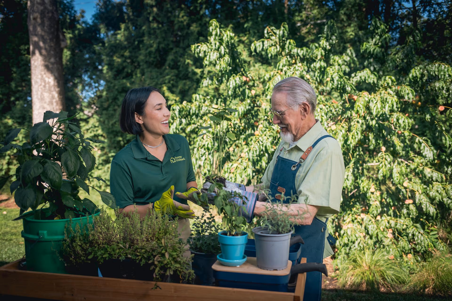Caregiver and resident gardening outdoors with potted plants.
