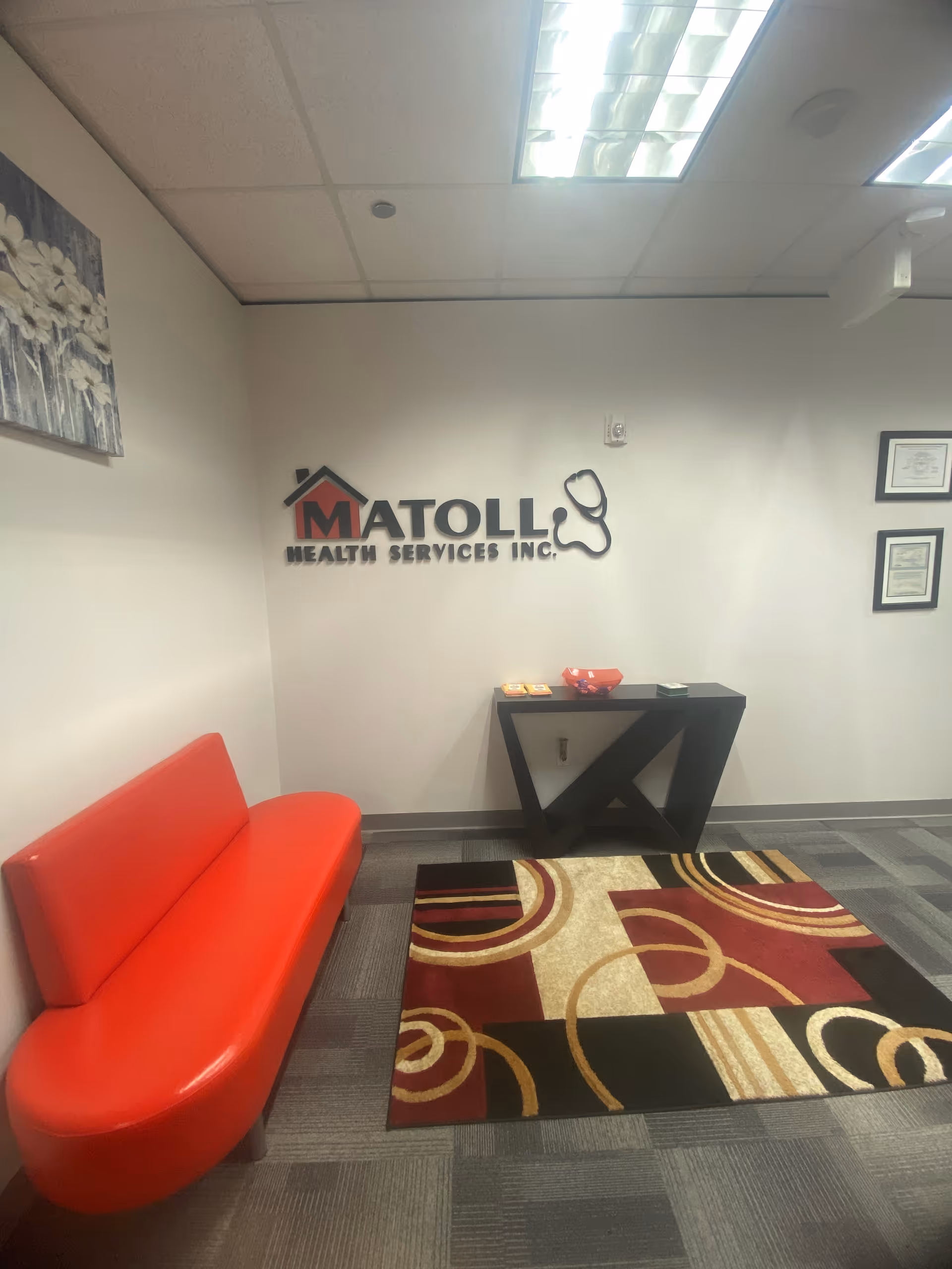 Lobby area with red bench seating, rug, and Matoll Health Services sign on wall.