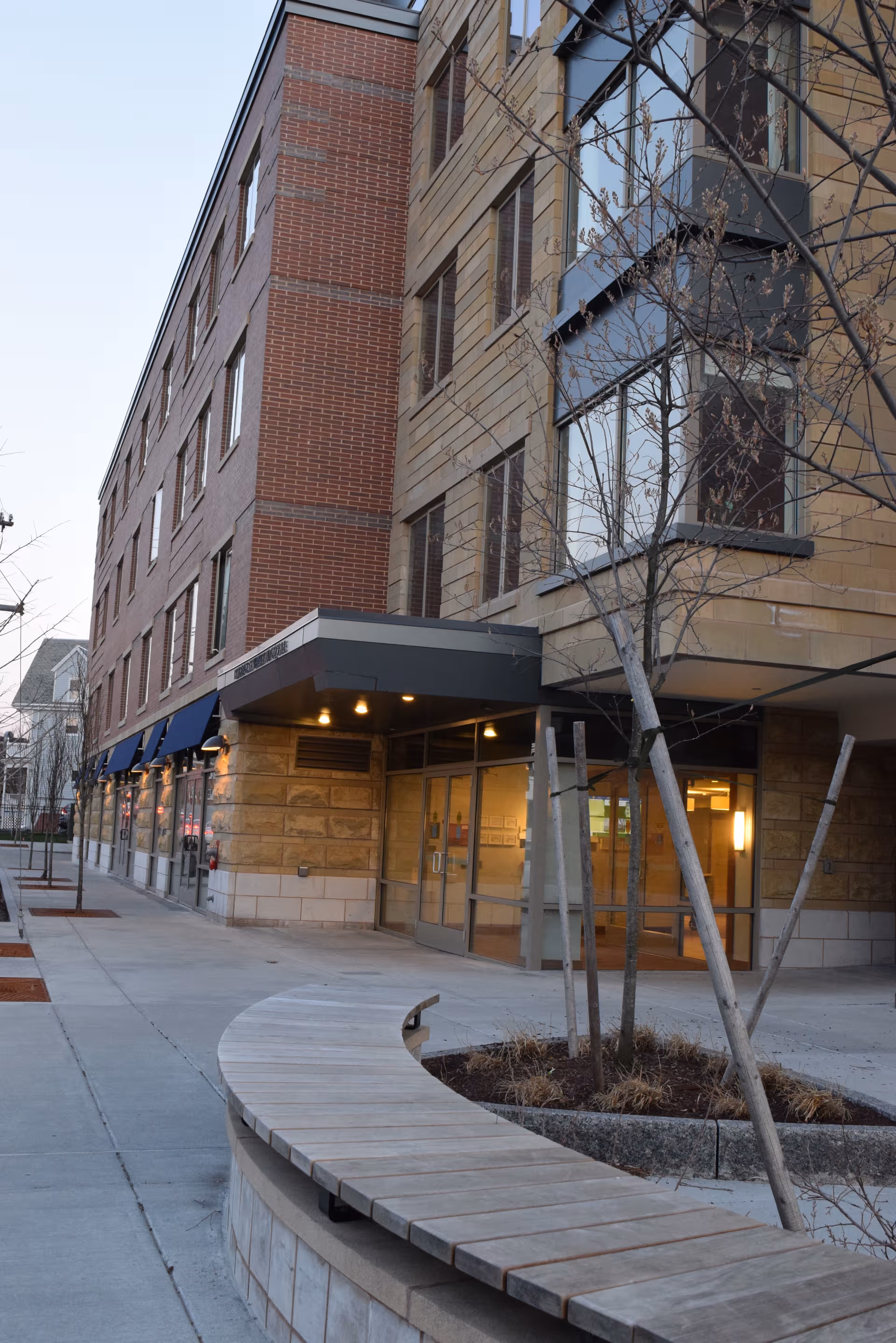 Exterior view of The Residence at Watertown Square entrance with curved wooden bench.