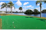 Artificial green lawn area with palm trees beside a water body under blue sky.