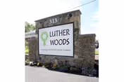 Stone entrance sign displays Luther Woods Nursing & Rehabilitation Center with surrounding landscaping.