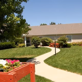 Sunny exterior of Brookdale Greeley with curved walkway, green lawn, and shrubs.