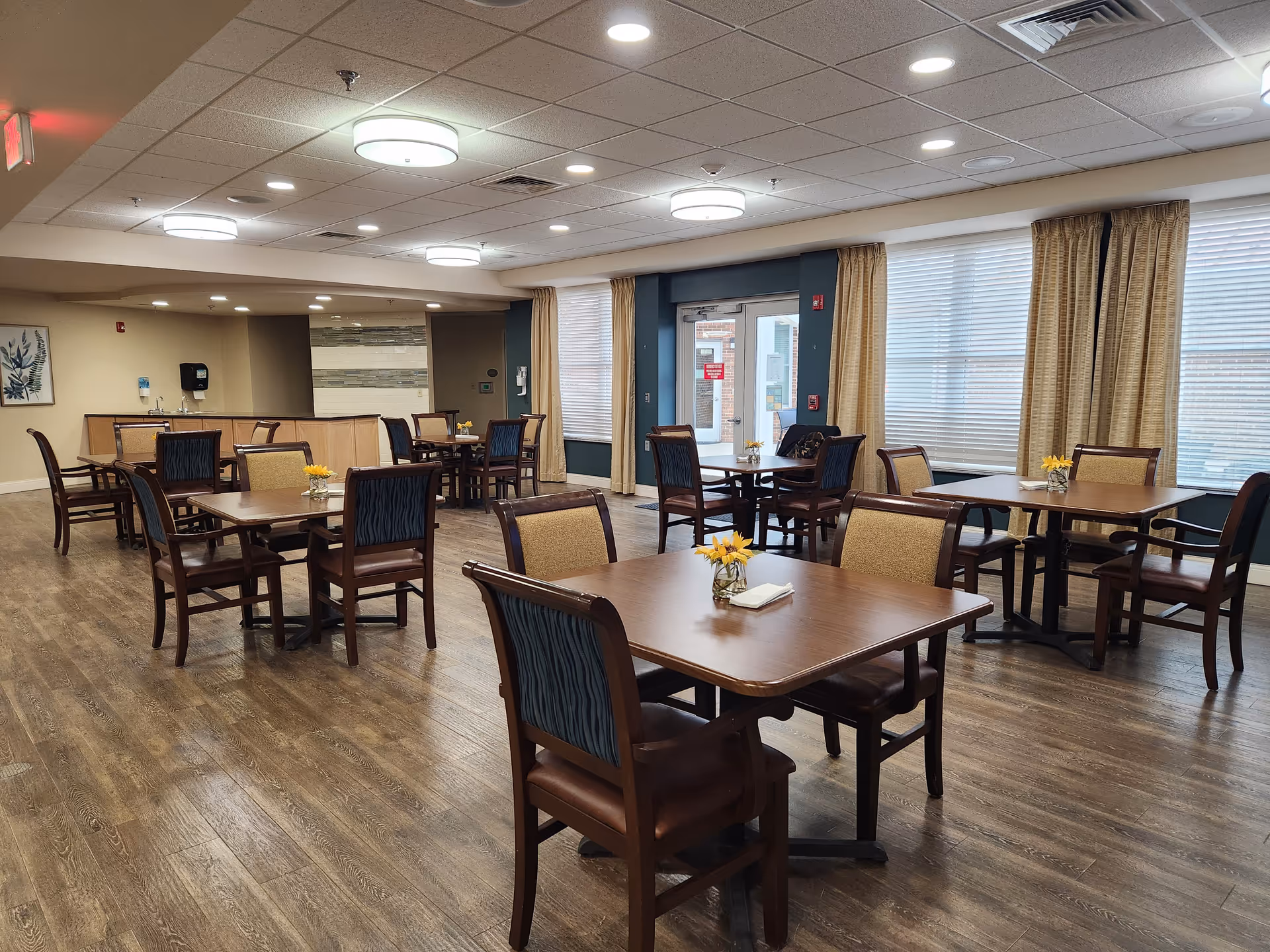 Spacious dining room with wood tables, chairs, and small yellow flowers.