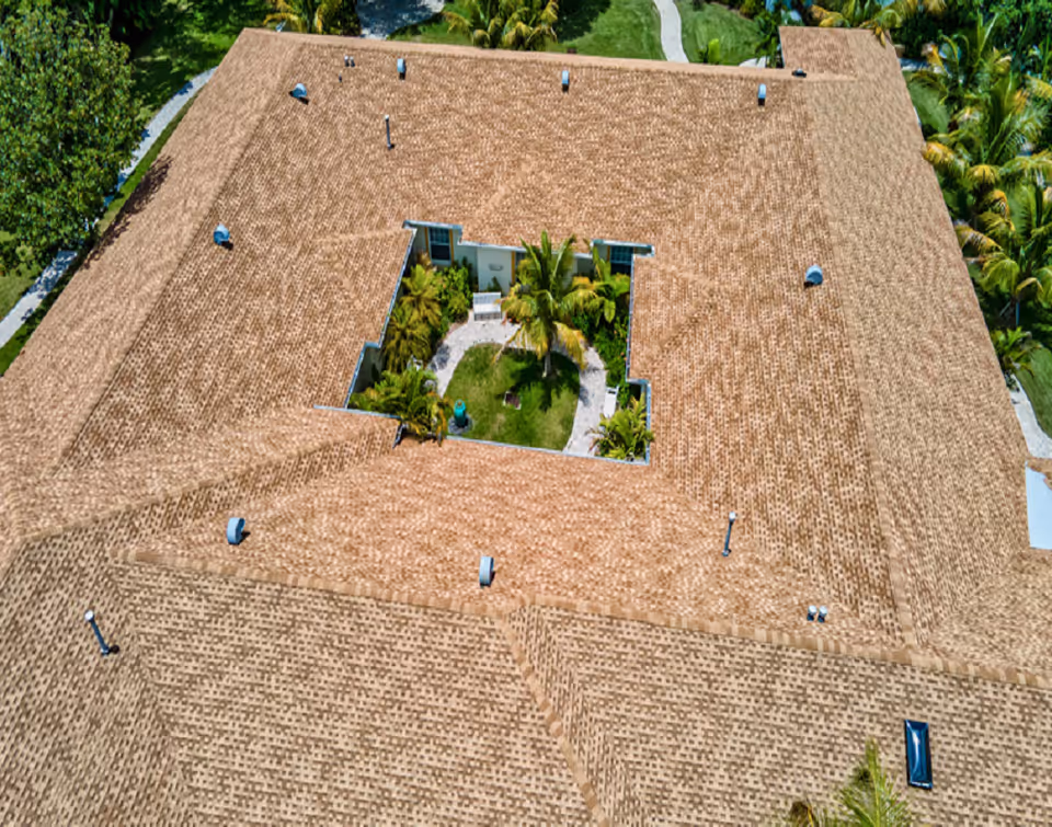 Aerial view of a large tan-tiled senior living facility with a central courtyard and palm trees.