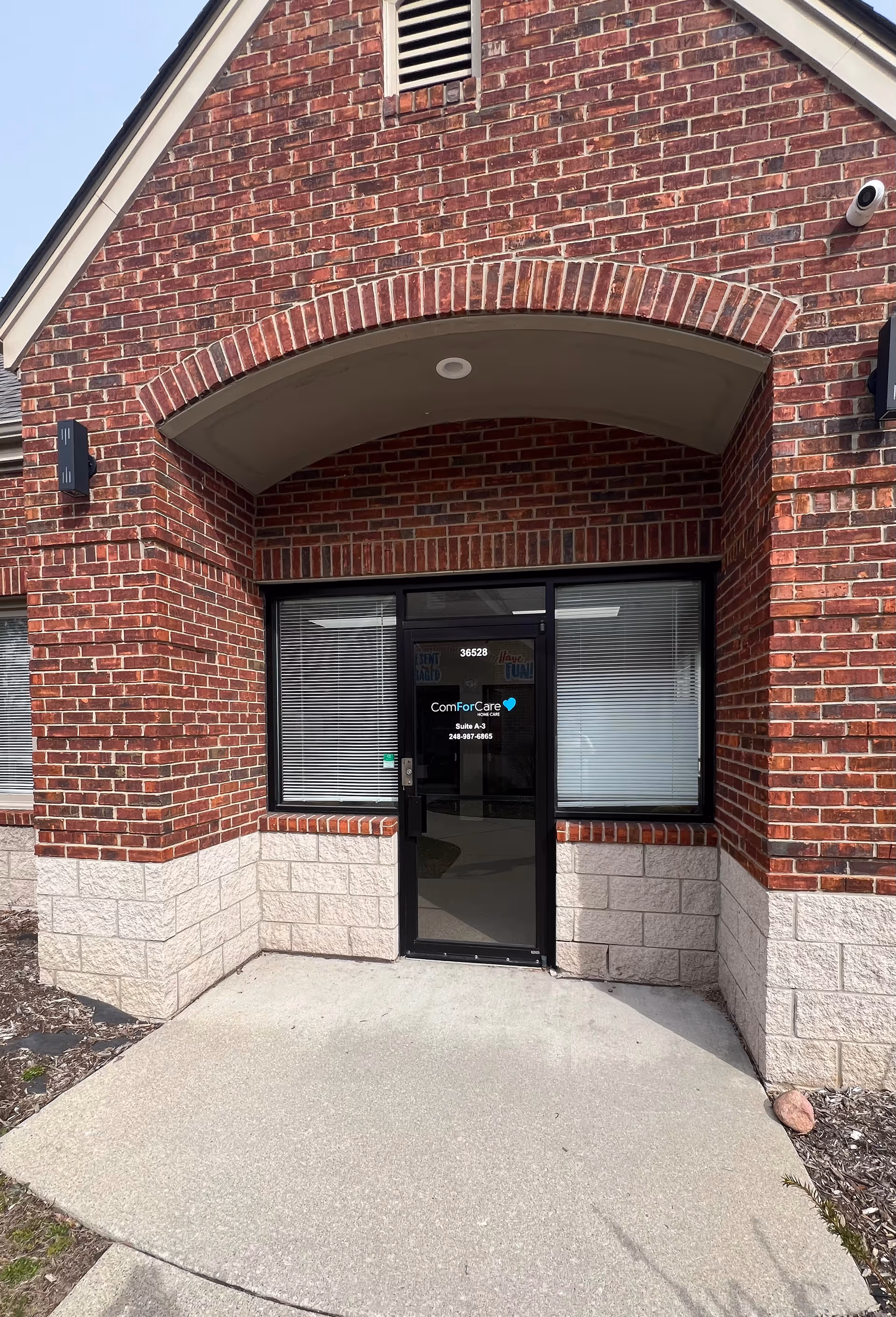 Brick building entrance with arched doorway and glass door labeled ComForCare.