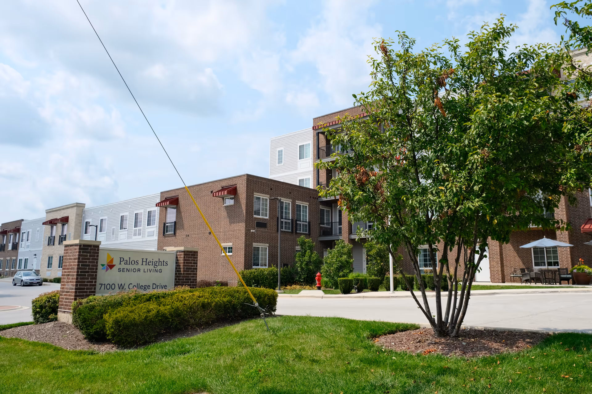 Exterior view of the Palos Heights Senior Living building and entrance sign with landscaping and a tree.