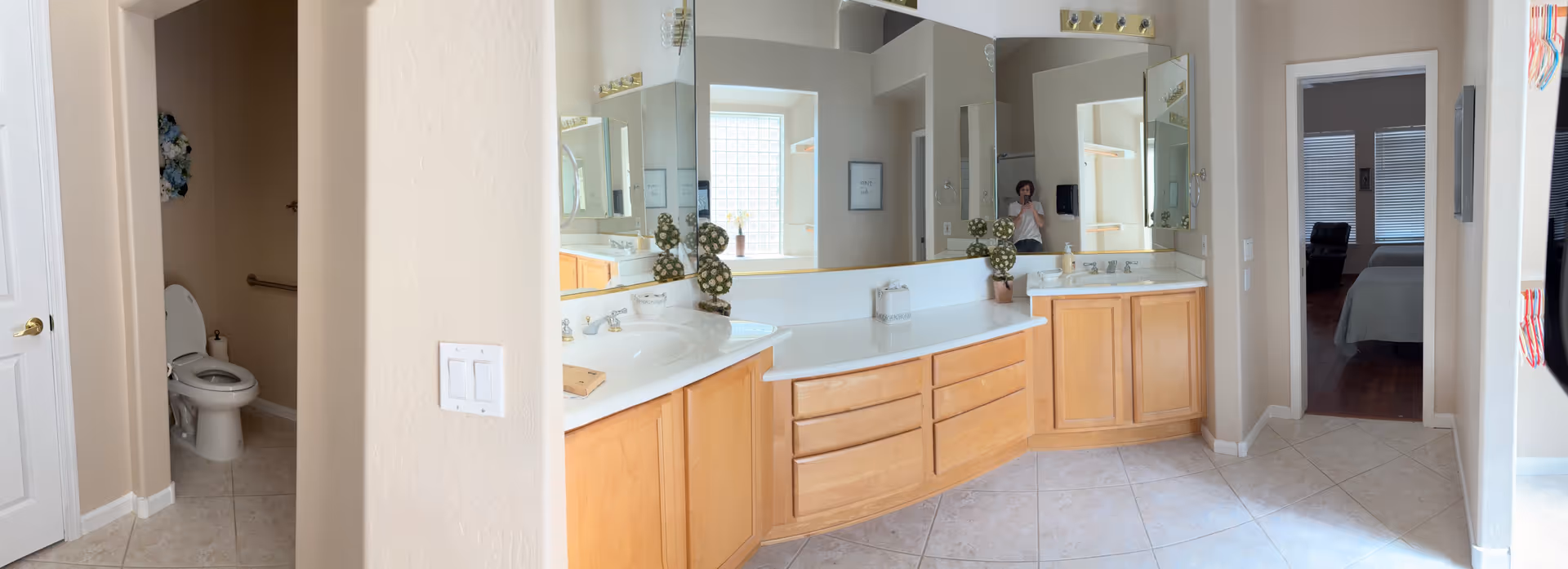 Wide bathroom vanity with multiple sinks and large mirrors inside an assisted living facility.