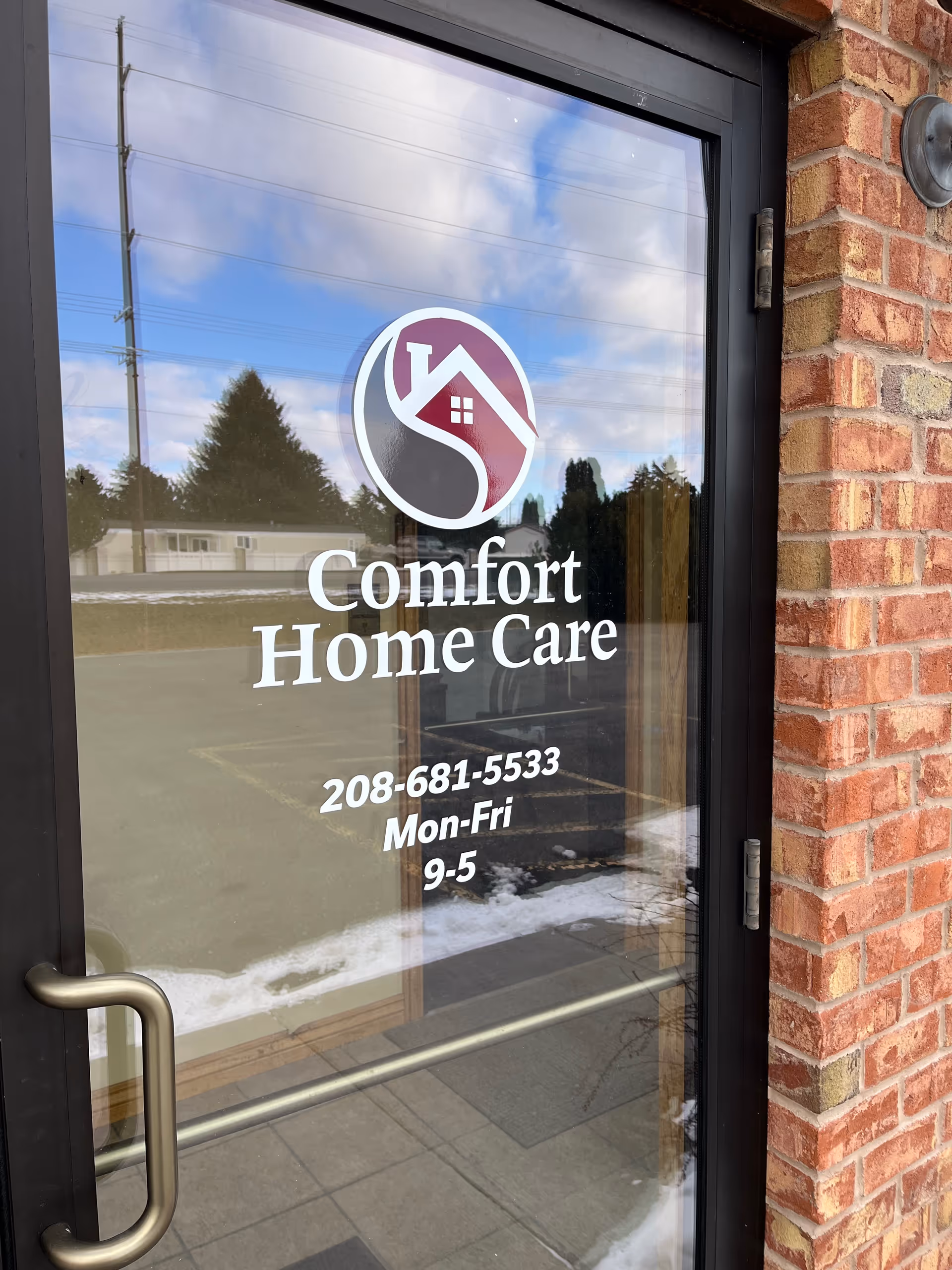 Glass door with Comfort Home Care logo and hours, brick exterior wall.