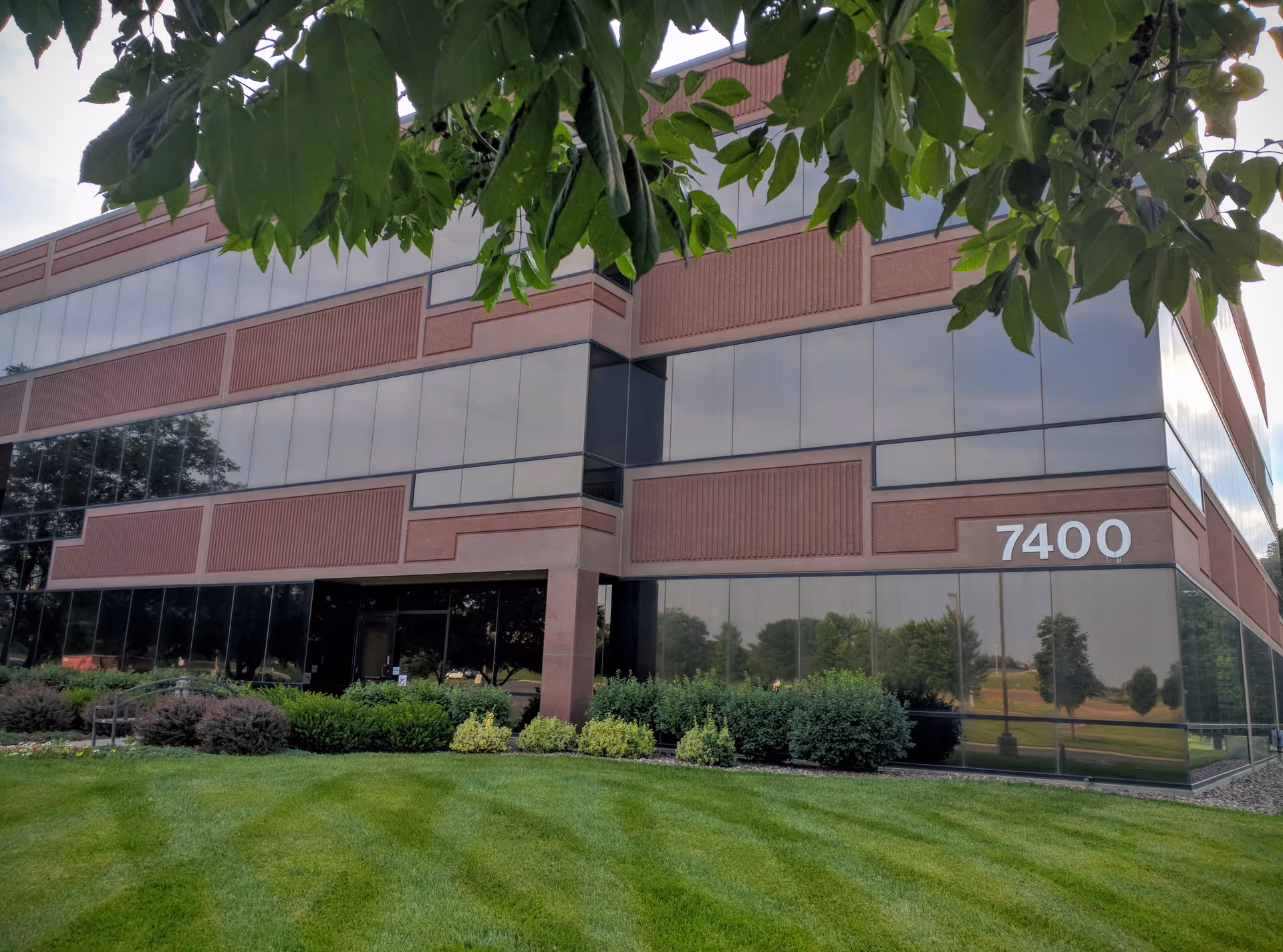 Modern brick-and-glass senior living facility exterior with manicured lawn and shrubs.