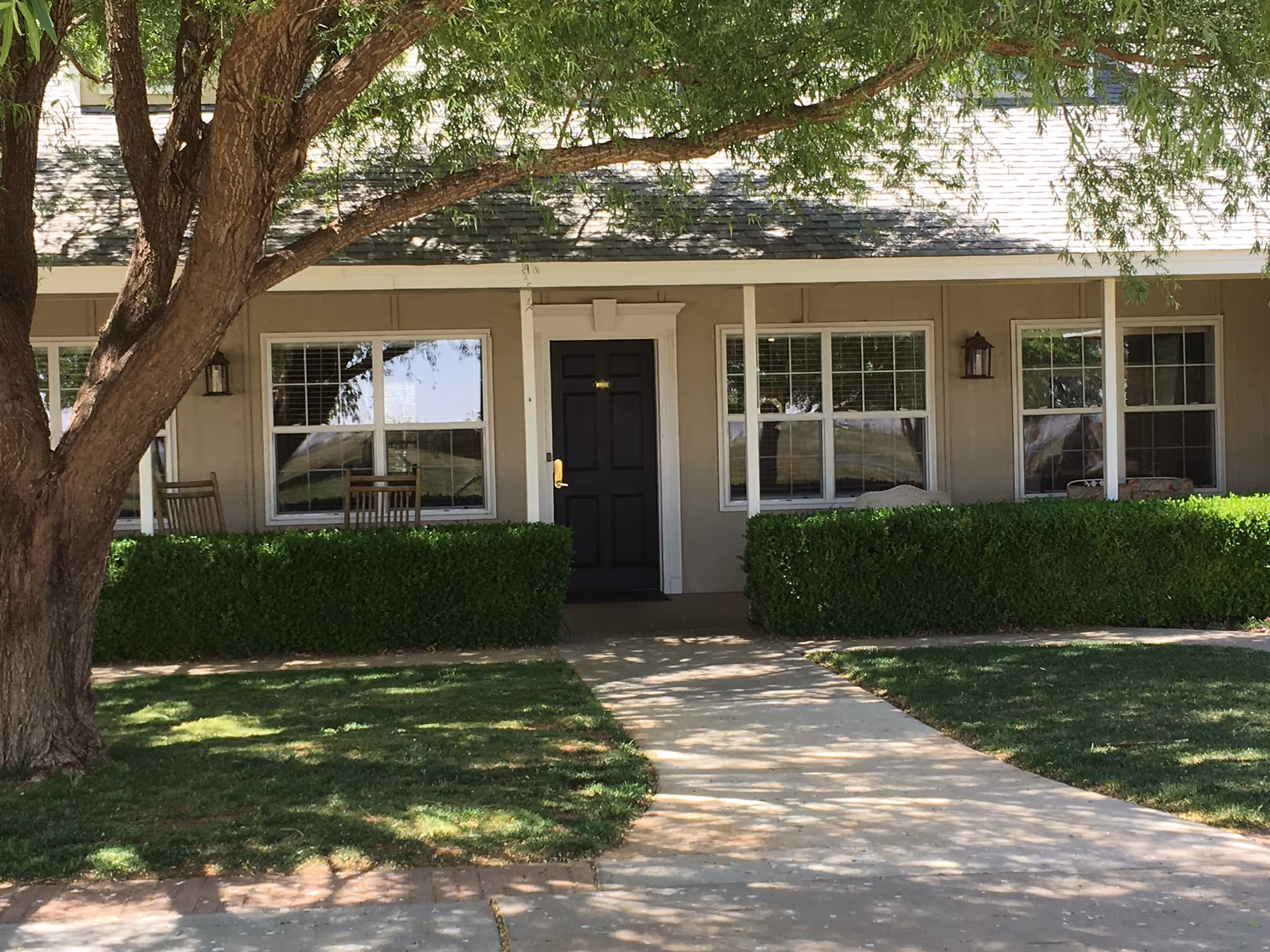 Single-story senior living facility front entrance with sidewalk, hedges, and porch seating.