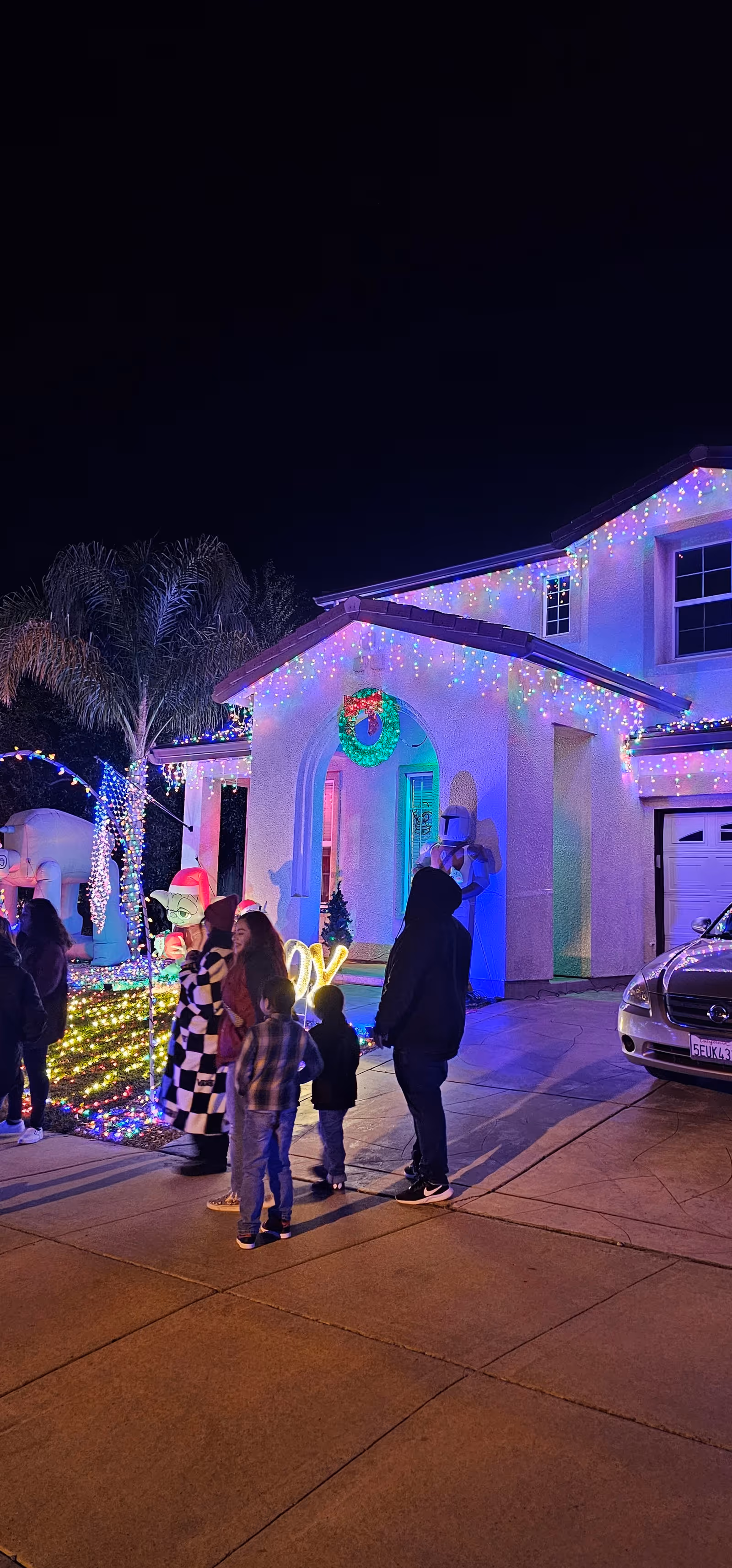 Night exterior of a house festively lit with Christmas lights and guests outside.