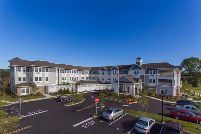 A large assisted living building with circular driveway, parking lot, and blue sky.