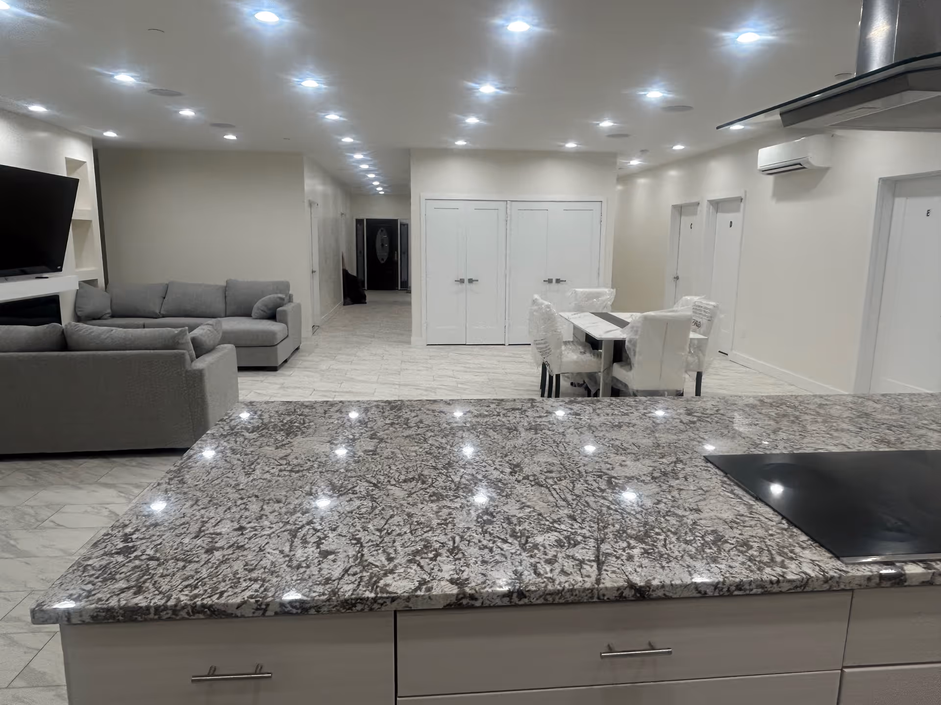 Spacious open-concept common area with granite kitchen island, dining table, and gray sofas.