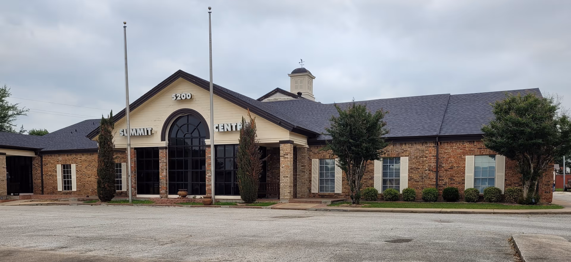 Brick facility exterior with central arched entrance and landscaped shrubs.