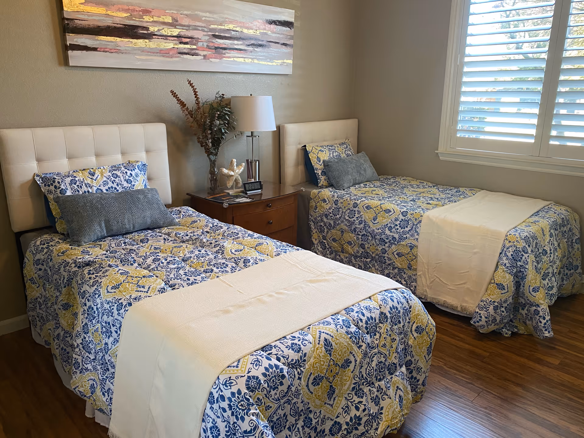 Two twin beds with matching blue and yellow quilts, a nightstand, lamp, and window.