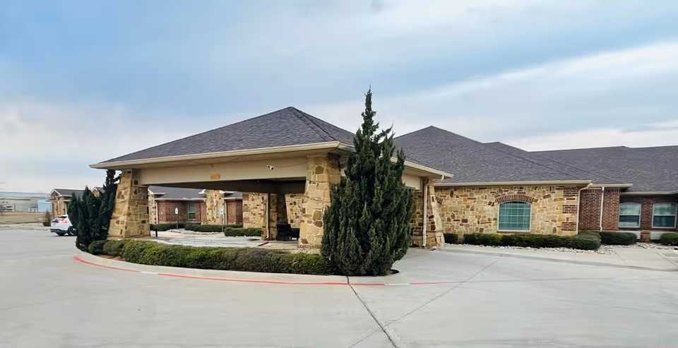 Single-story stone and brick senior living facility exterior with a covered porte-cochere, driveway, and landscaping.
