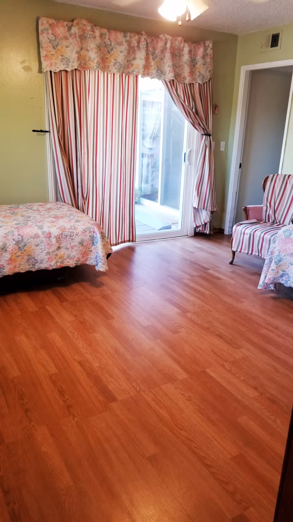Bright bedroom with floral bedding, striped curtains, and sliding glass door to a patio.