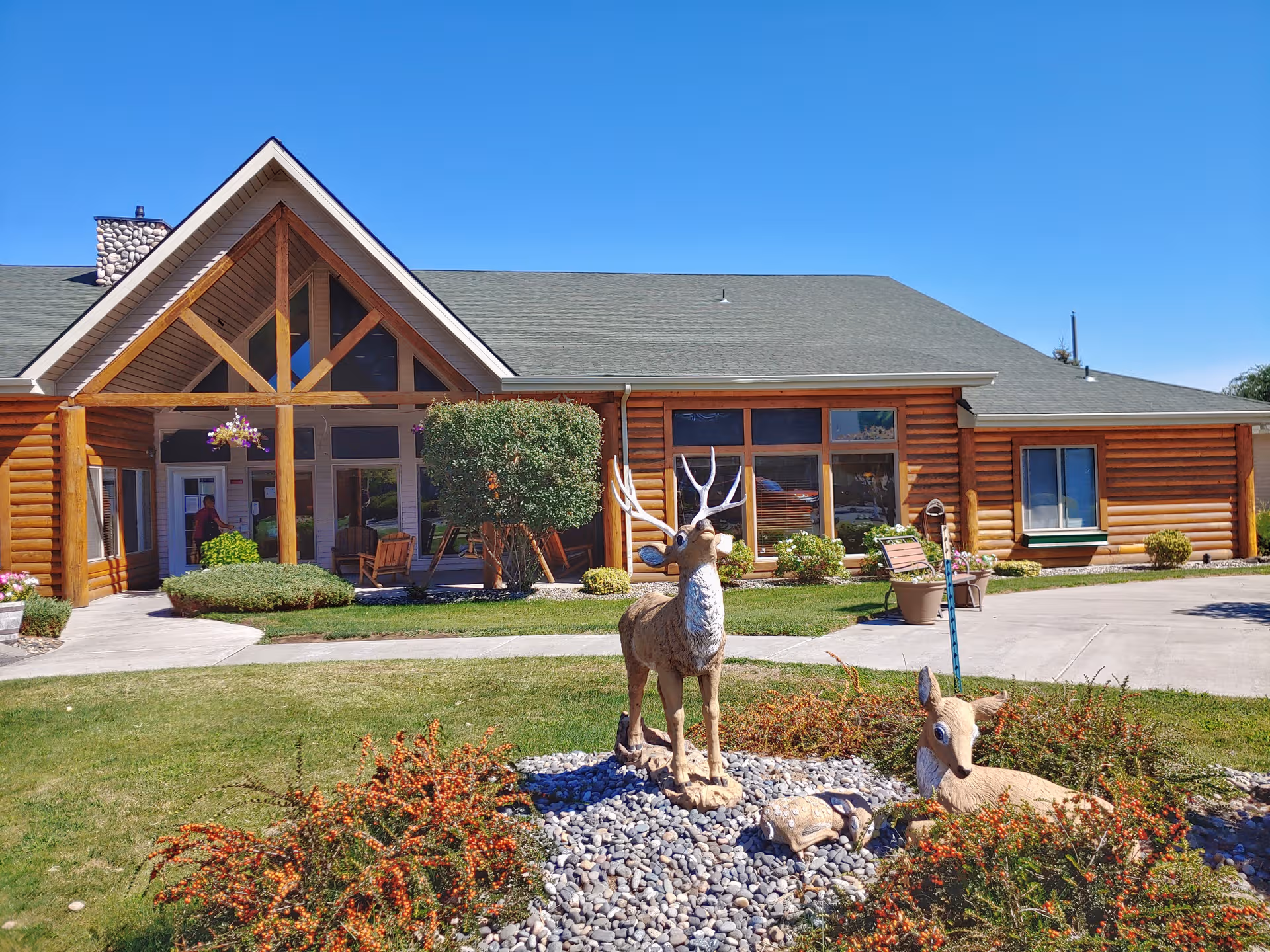 Log-style senior living facility facade with landscaped front yard and deer sculptures.