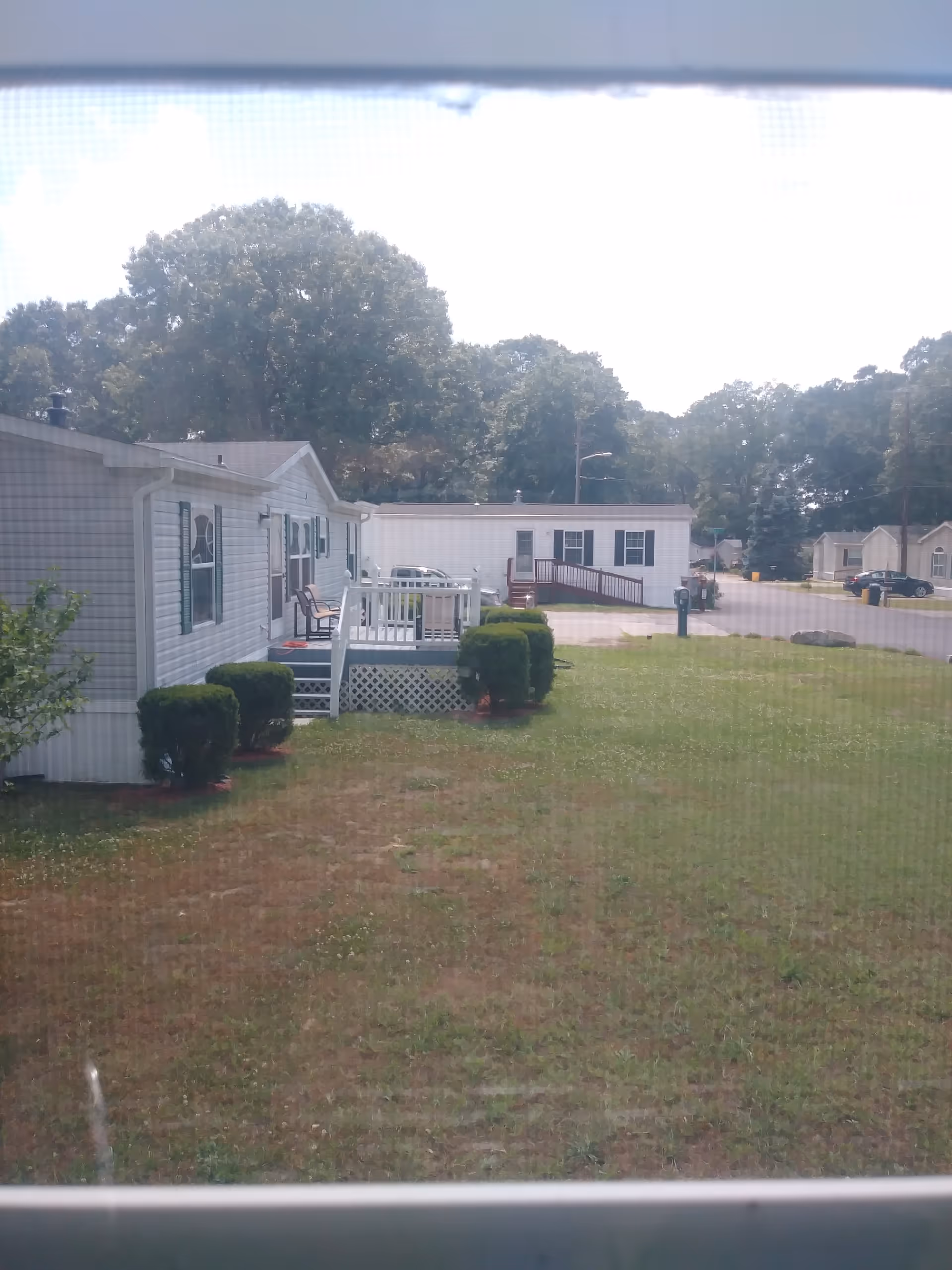 Exterior view of mobile homes with small porches, shrubs, and a grassy lawn.