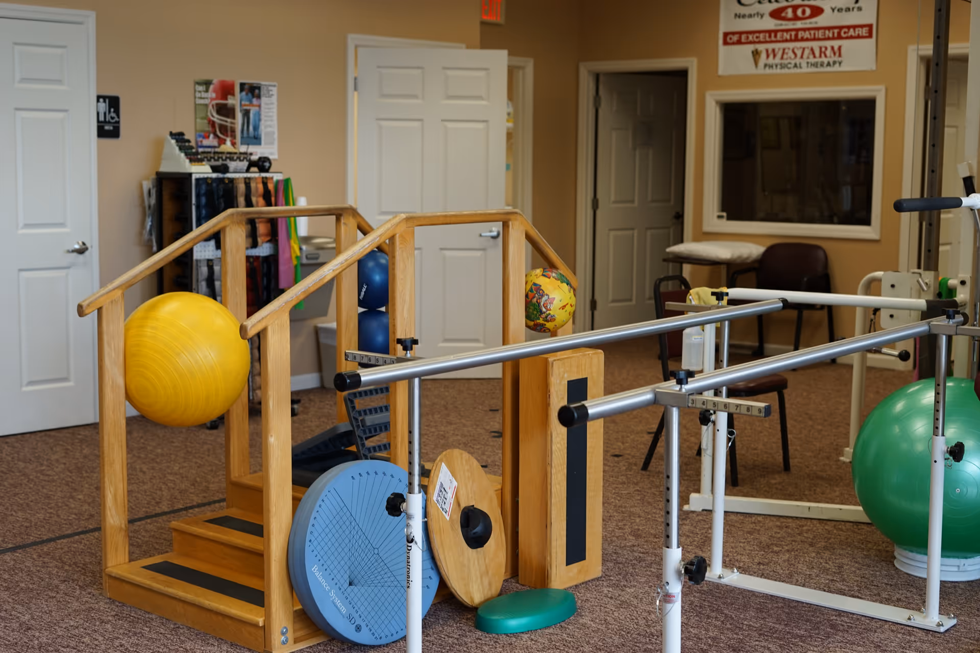 Interior rehab gym with wooden parallel bars, balance equipment, and therapy balls.