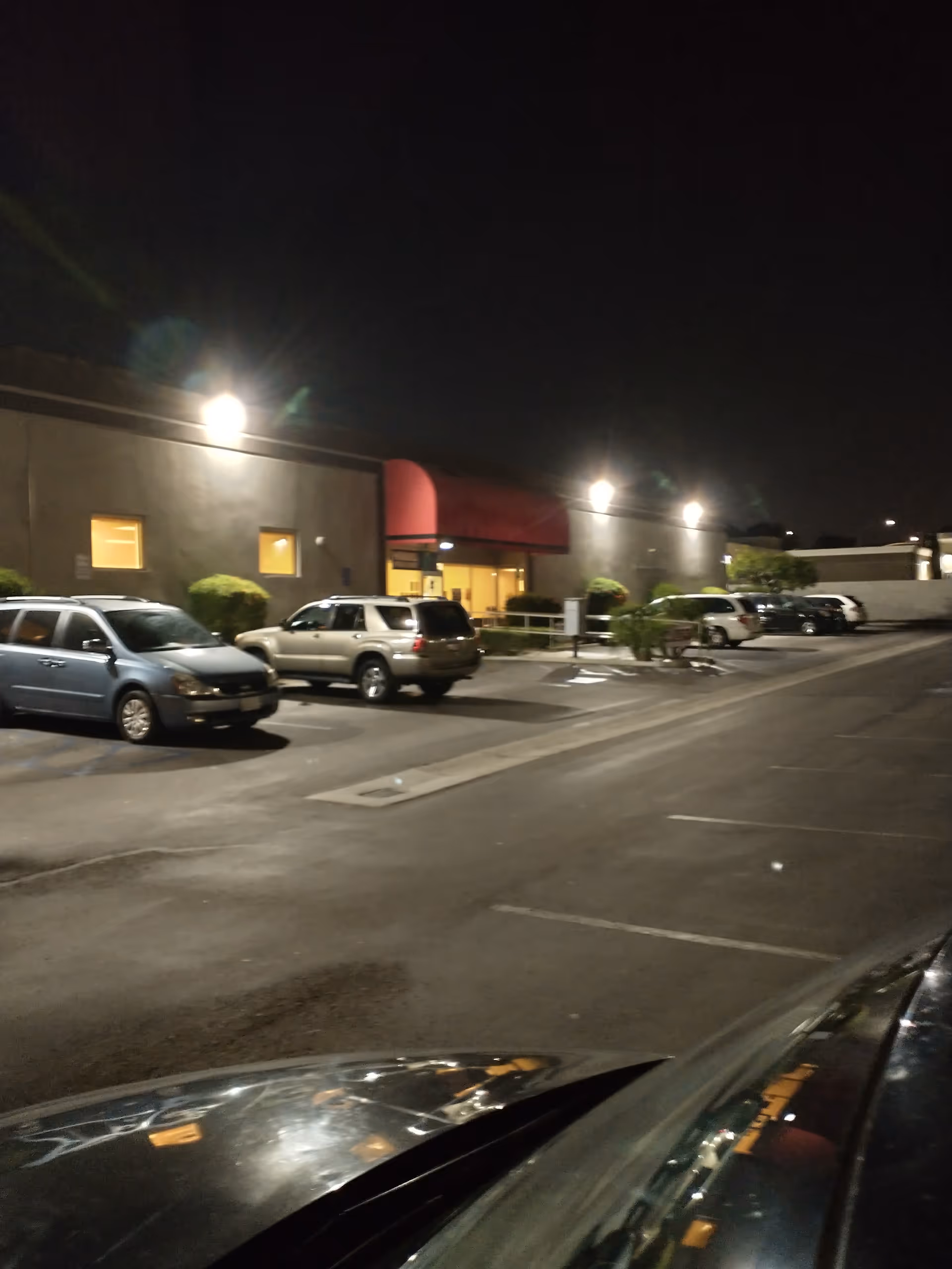 Night exterior of a senior living facility with a lit entrance and parked cars.