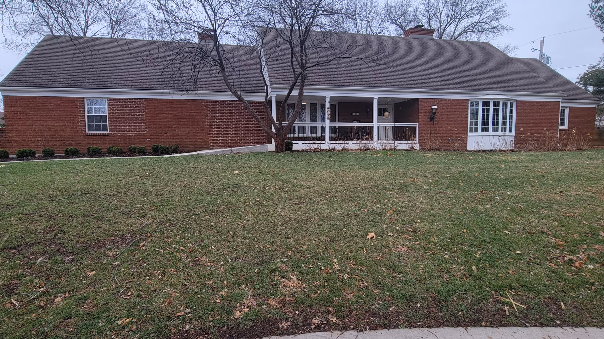 This single-story red brick memory care home features a covered front porch and lawn.