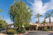 A single-story senior living facility with a covered entrance and palm trees.