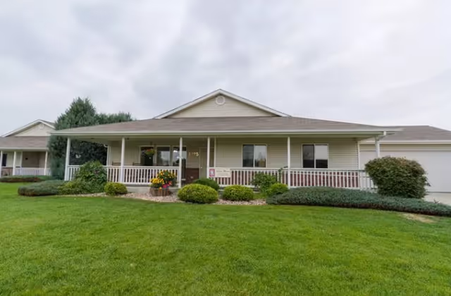 Front of a single-story senior living building with a porch, lawn, and trimmed shrubs.
