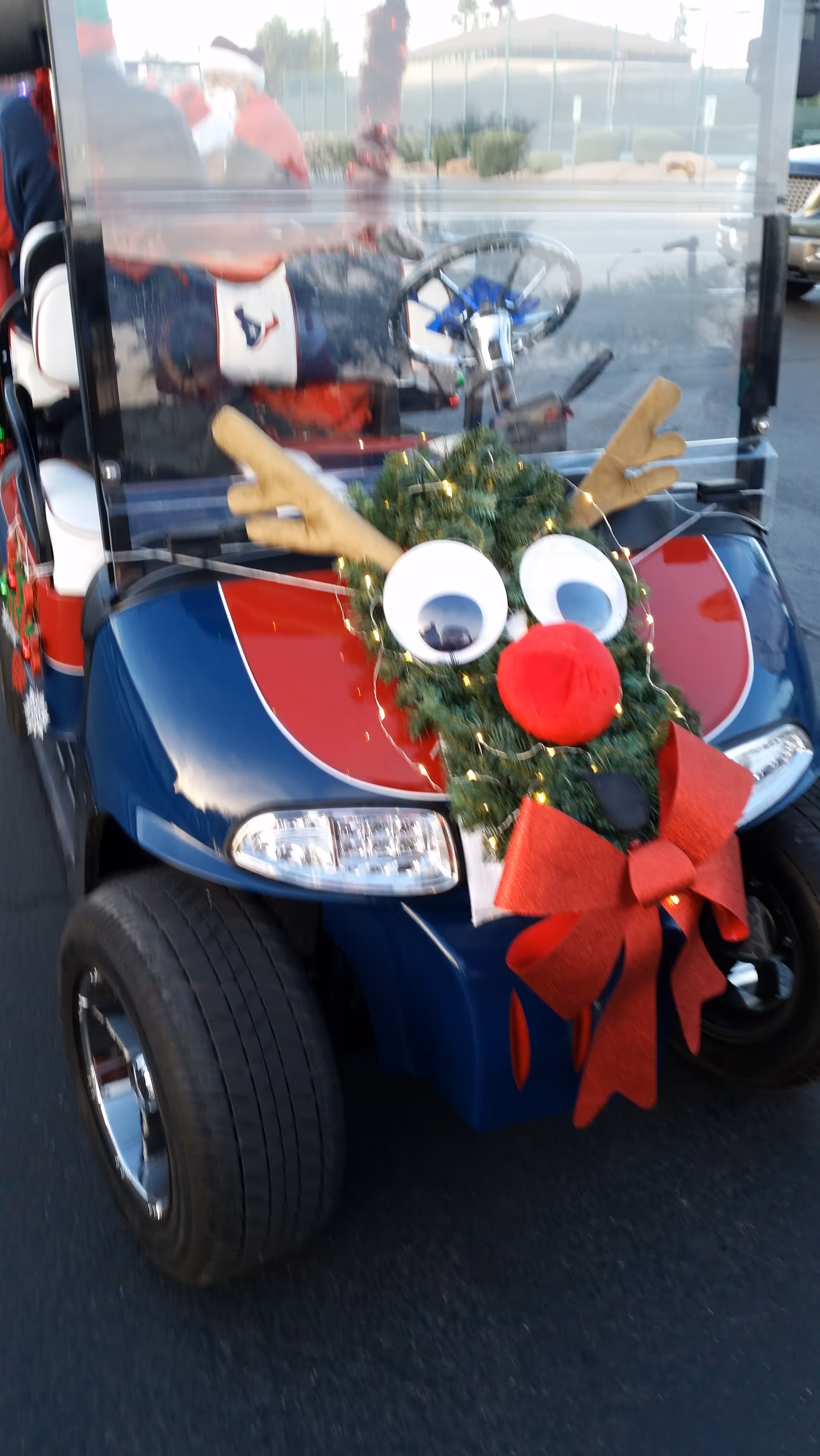Decorated golf cart with wreath, googly eyes, antlers, and red bow outdoors.