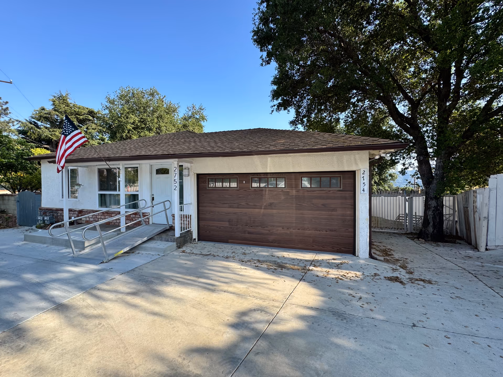 Small single-story facility with a two-car garage, ramp, flag, and trees.