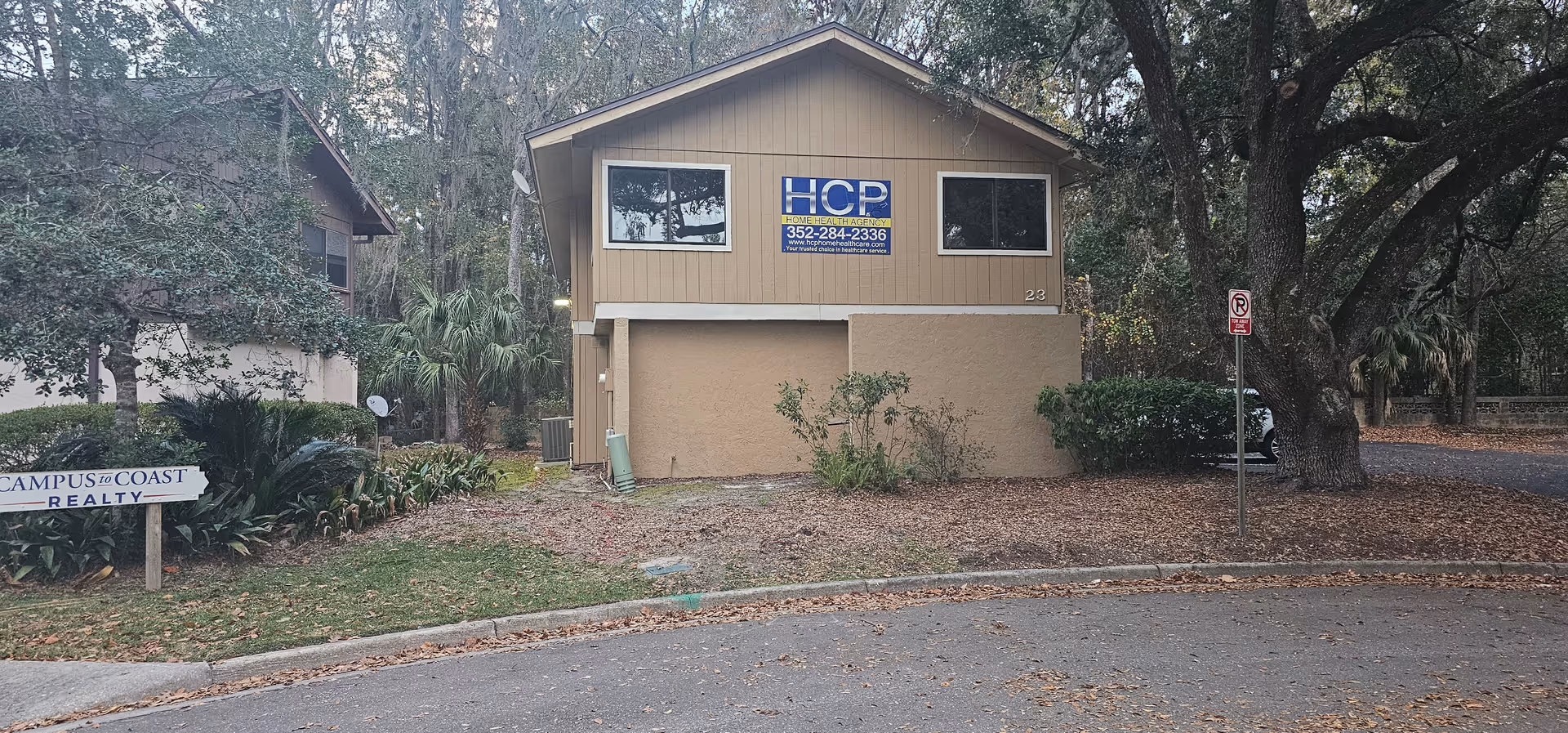 A beige two-story building with an HCP Home Healthcare Agency sign beside trees.