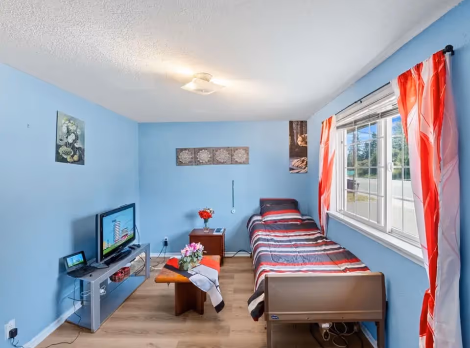 Blue bedroom with single bed, window, TV, and small table with flowers.