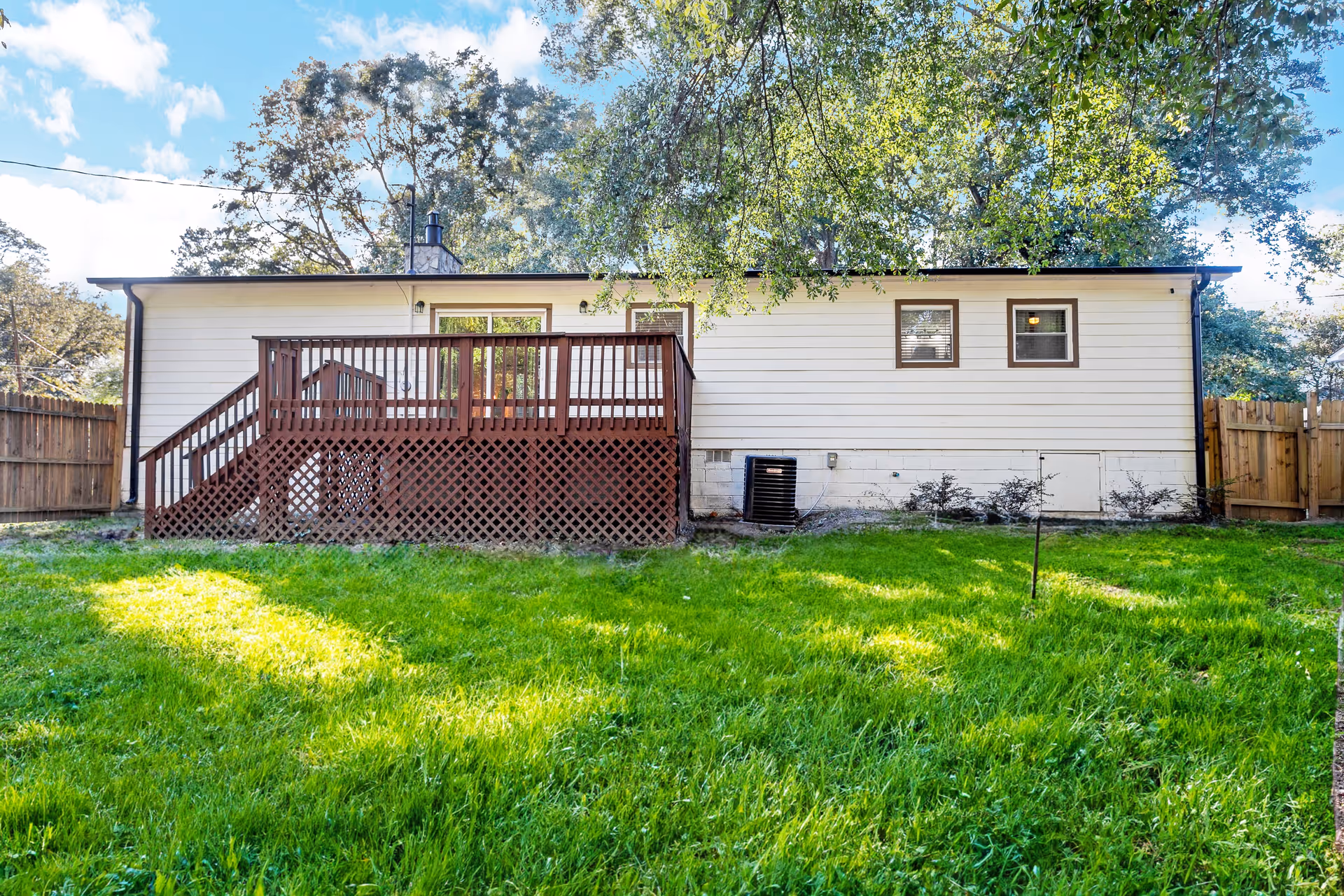 A single-story building with a wooden deck, fenced yard, and lush green lawn.