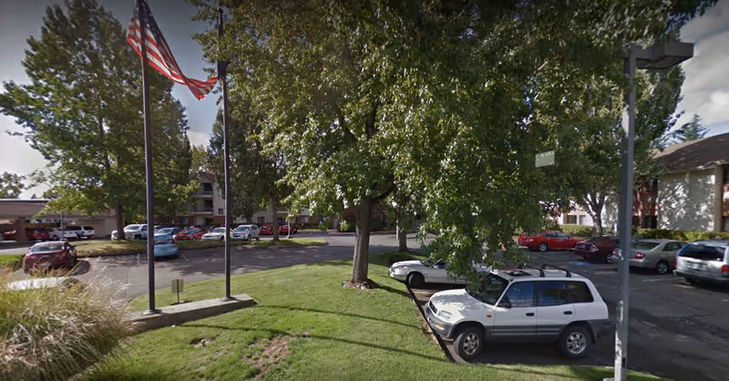 Exterior view of Cornell Estates senior living facility with parked cars, flagpoles, trees, and a lawn