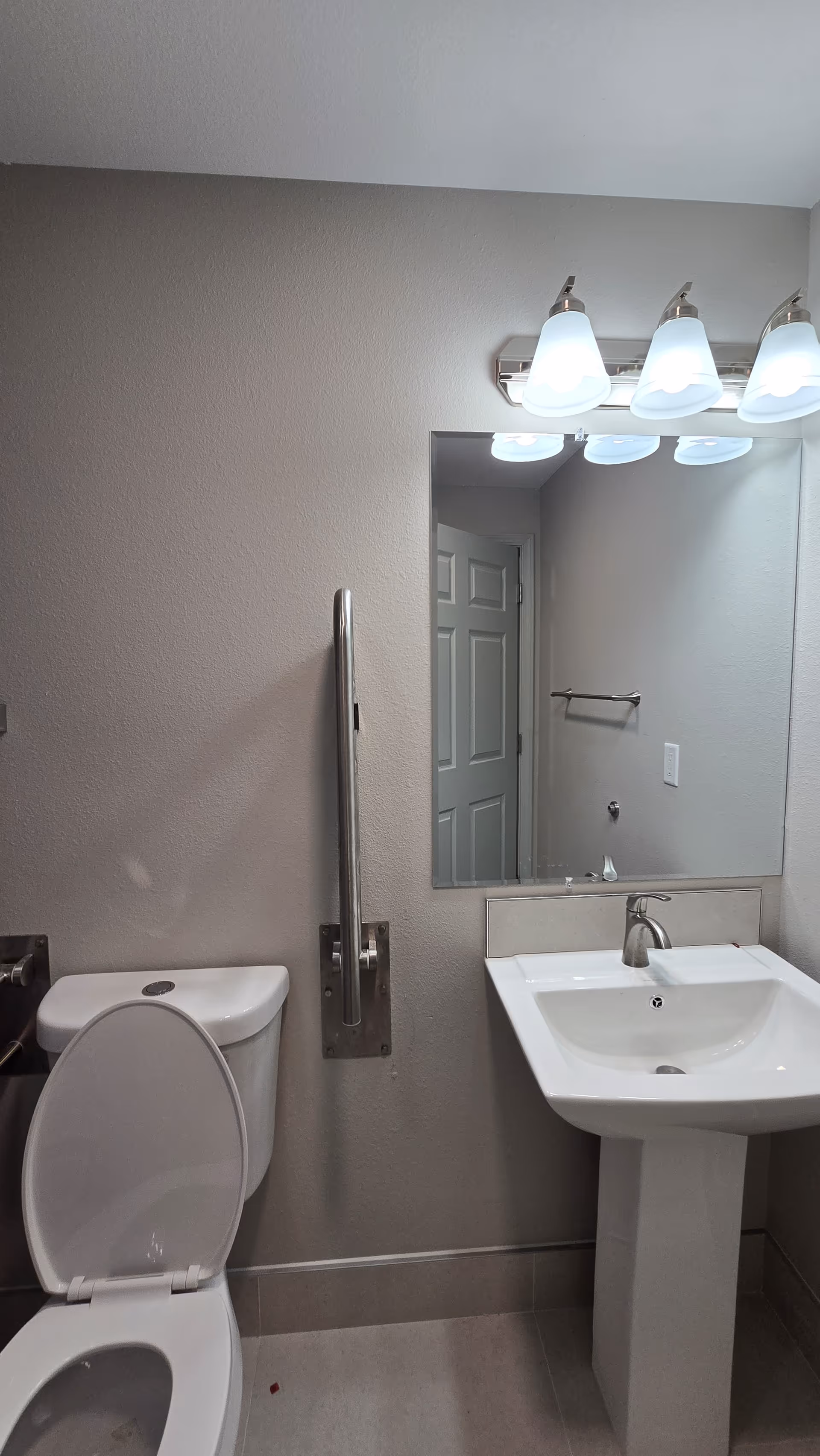 Bathroom featuring a toilet, pedestal sink, mirror, overhead lights, and a wall-mounted grab bar.