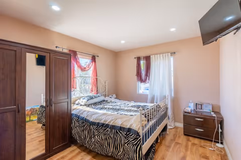 Bright bedroom with a zebra-pattern bed, dark wooden wardrobe, nightstand, and wall-mounted TV.