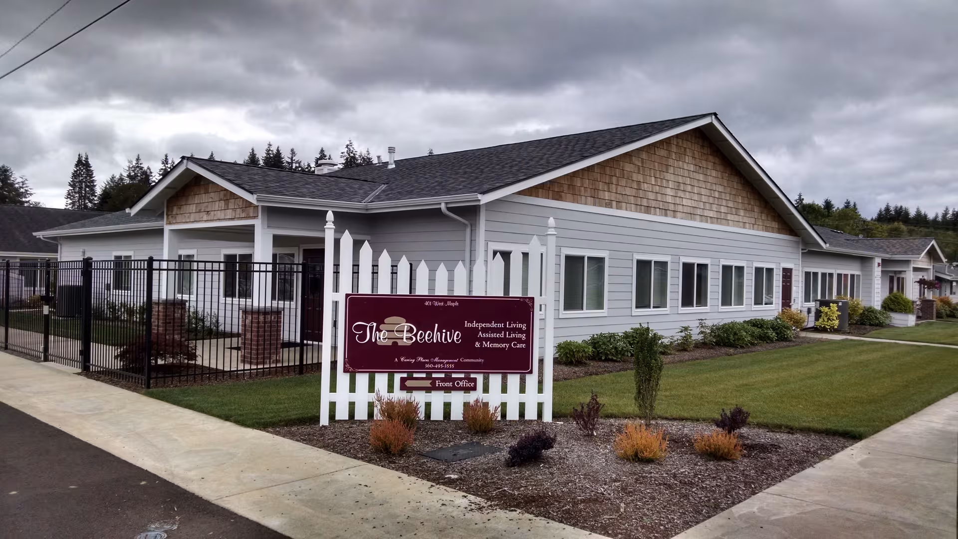 Exterior view of The Beehive Retirement Community building with a white picket sign in front