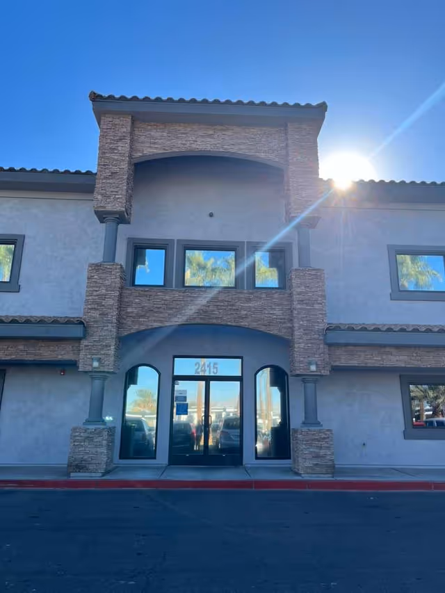 Sunlit exterior of a senior living facility with arched glass entrance and stone accents