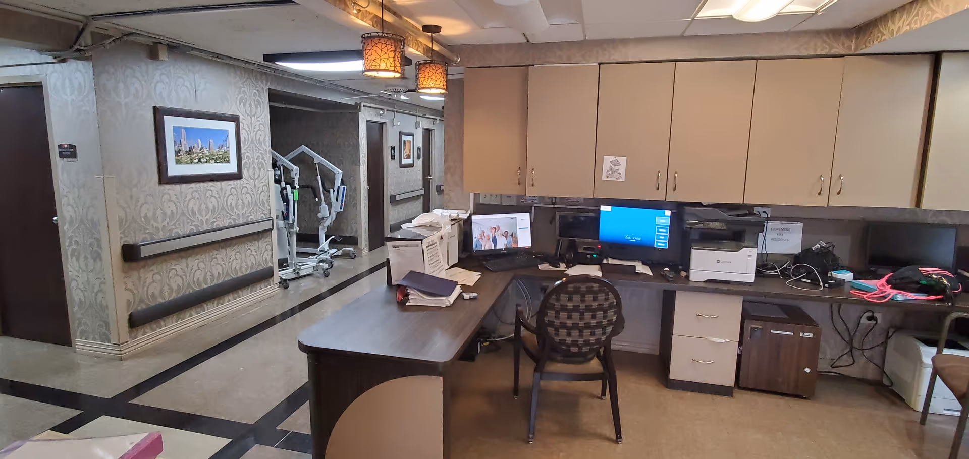Reception desk with computer, printer, and storage cabinets in a senior living facility interior.