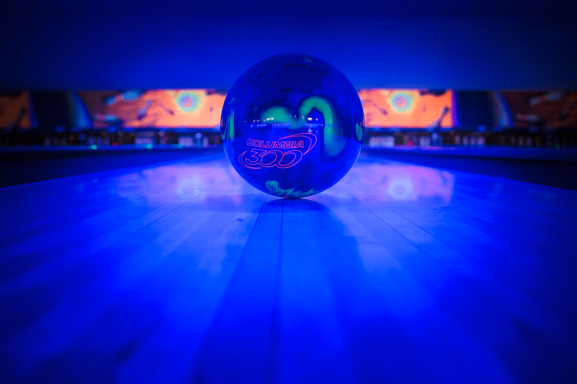 Blue-lit bowling ball rests on a polished lane in a neon-lit bowling alley.
