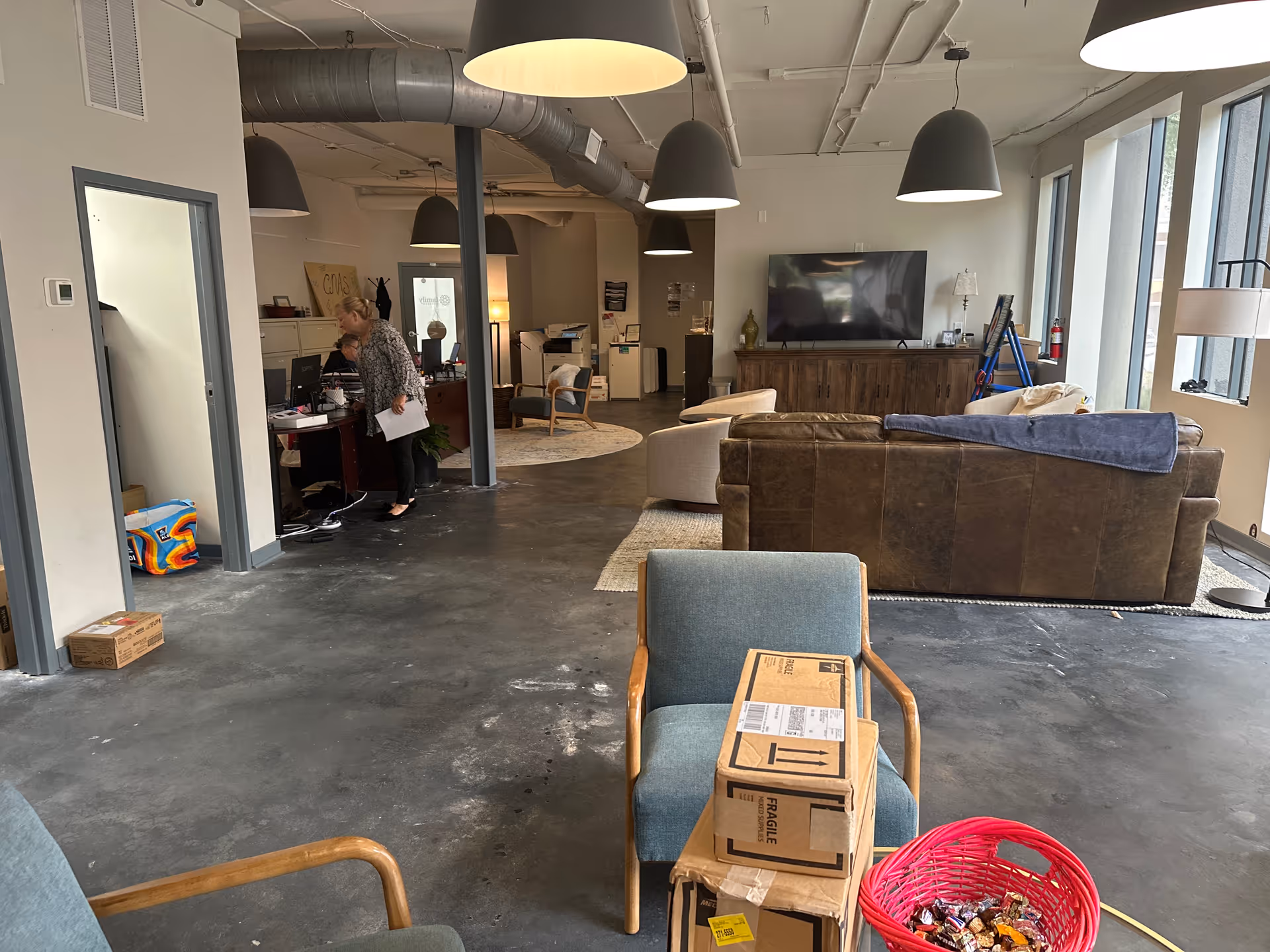 Industrial-style common living area with sofas, a TV, desk, and large windows.
