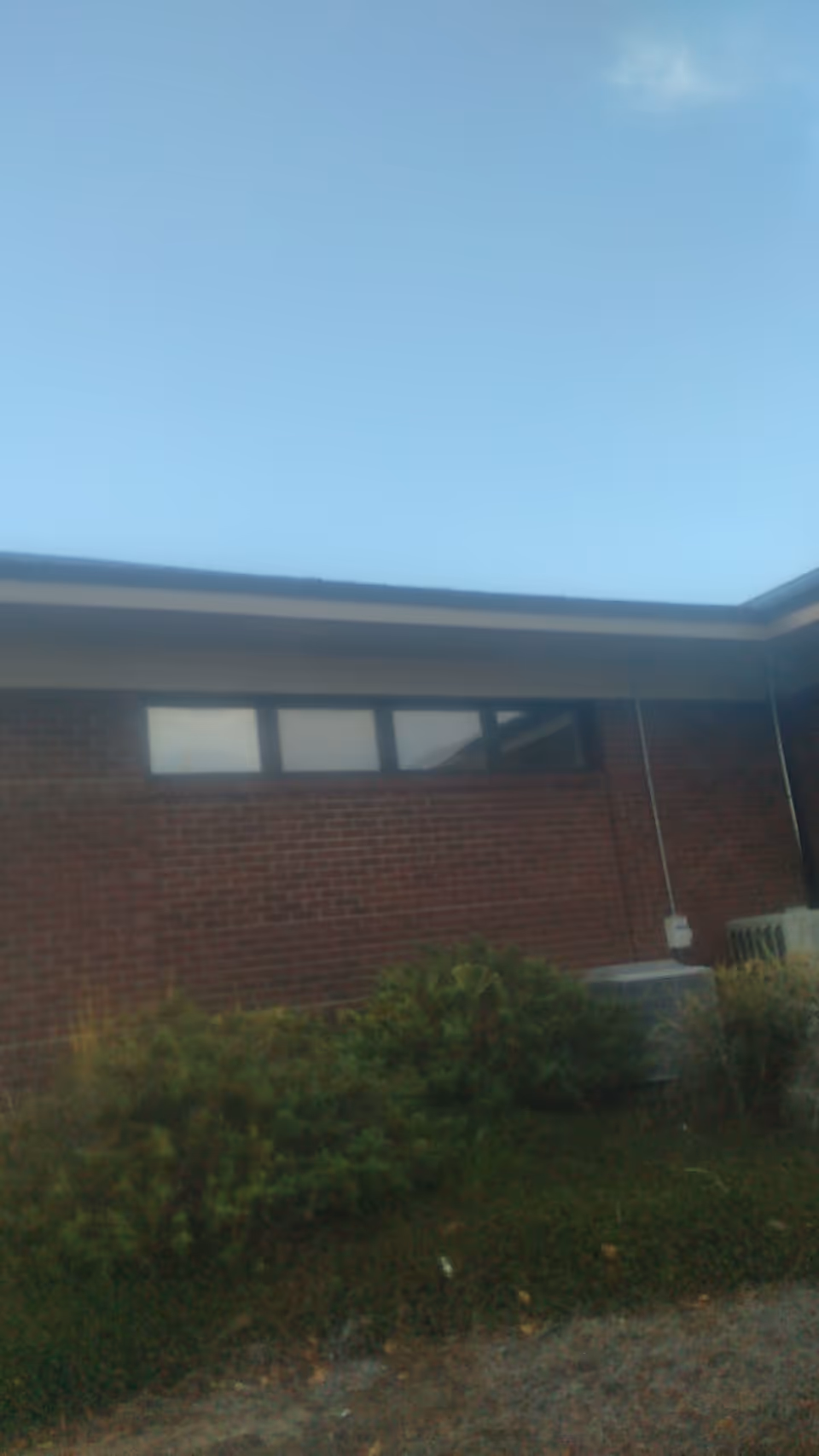 Exterior view of a brick facility with windows and shrubs outside.