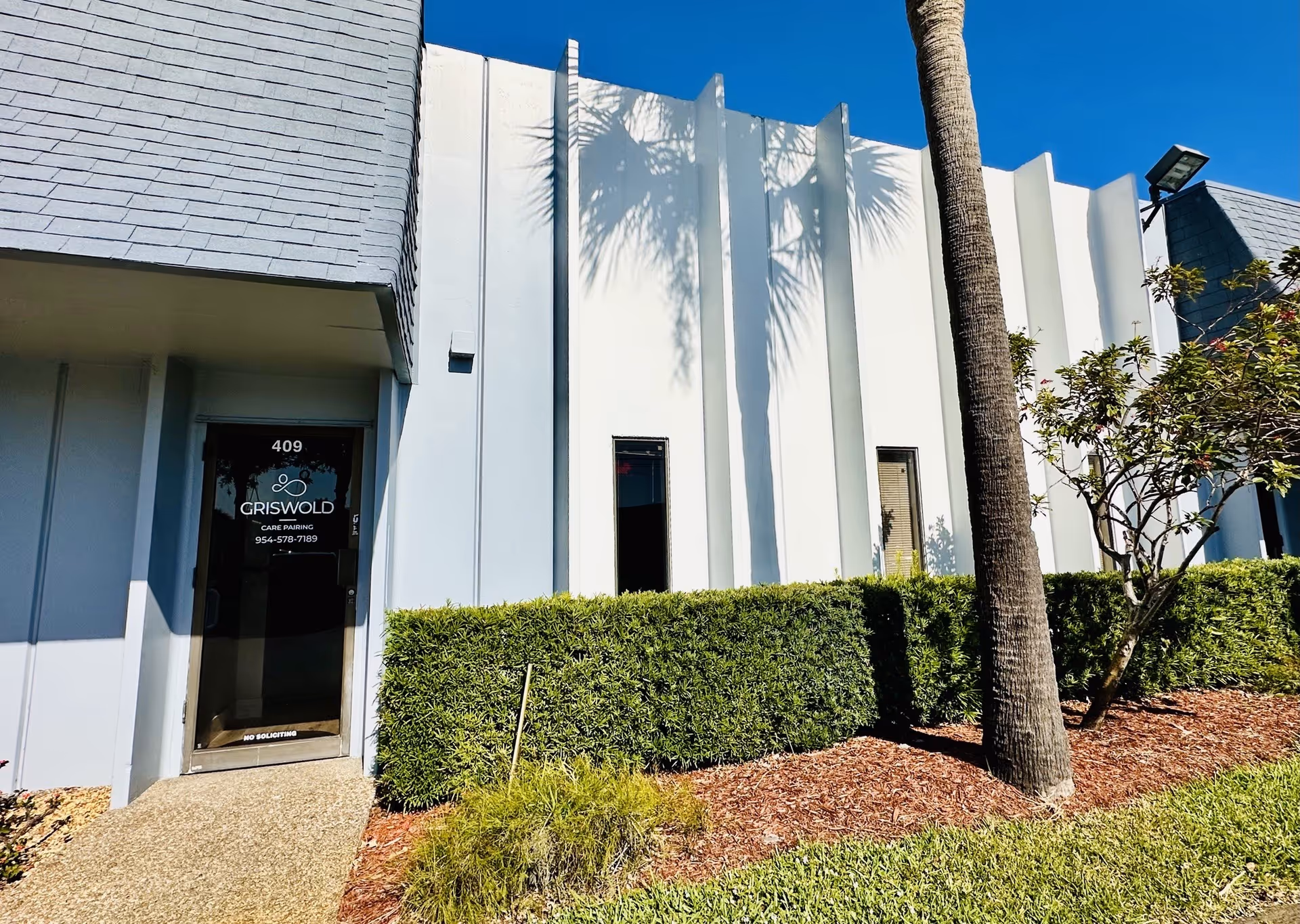White modern facility exterior featuring a glass door labeled Griswold and hedged landscaping.