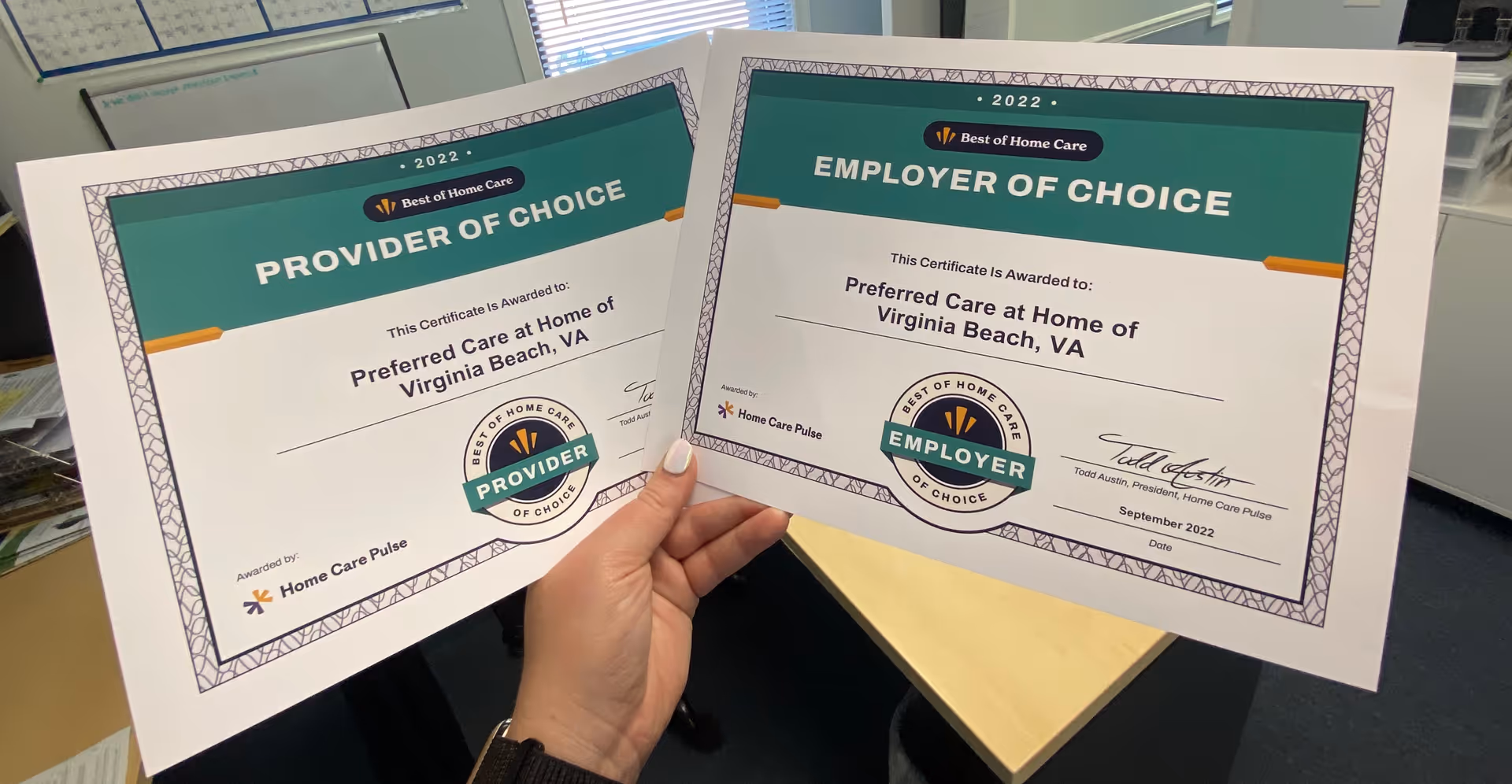 Two certificates held by hands inside an office for Preferred Care at Home of Virginia Beach.